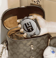 A hand placing the compact, fully folded phone stand into a woman's handbag, showcasing its pocket-sized design and portability for travel.