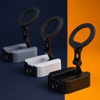 Three foldable magnetic phone stands displayed in a row, showcasing the available color options: all-black, white with black accents, and silver with black accents, set against a stylish split-color background.